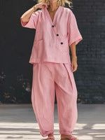 Person wearing a pink outfit with black buttons against a dark brick wall.