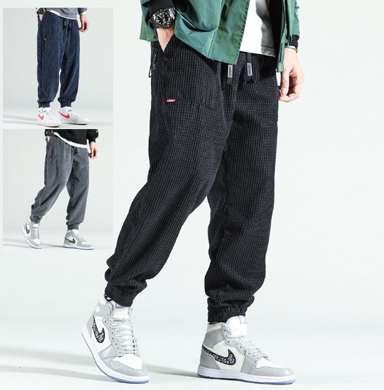 Person wearing black corduroy jogger pants with a green jacket and white sneakers on a white background.