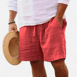 Person wearing red shorts and a white shirt, holding a straw hat on a plain background