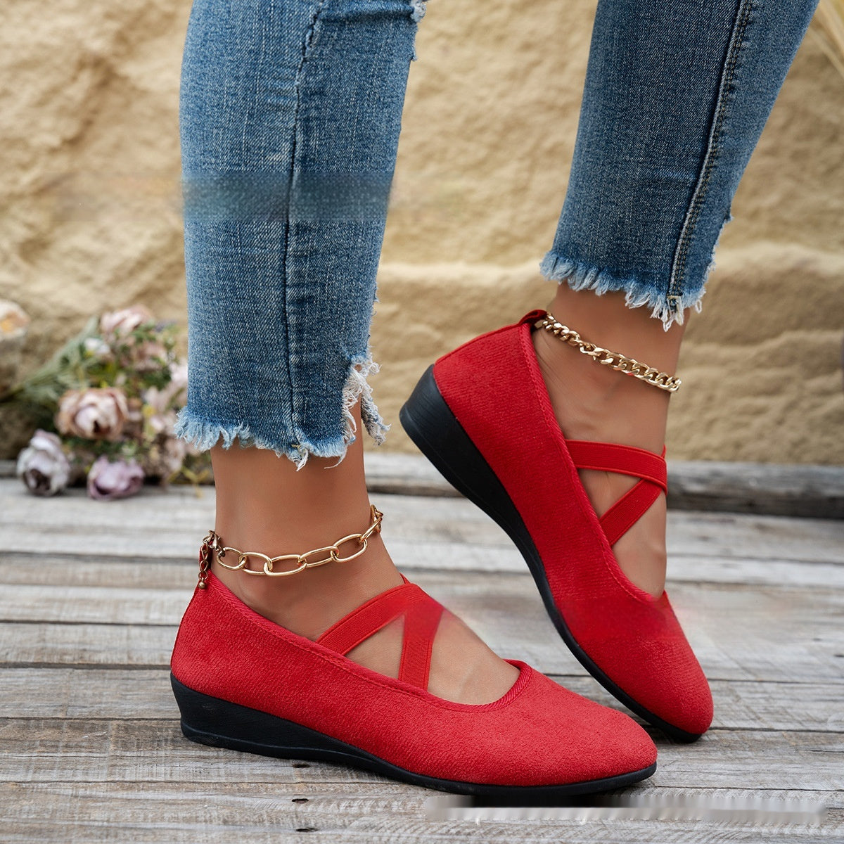 Red shoes with black soles worn with blue jeans on a wooden floor.