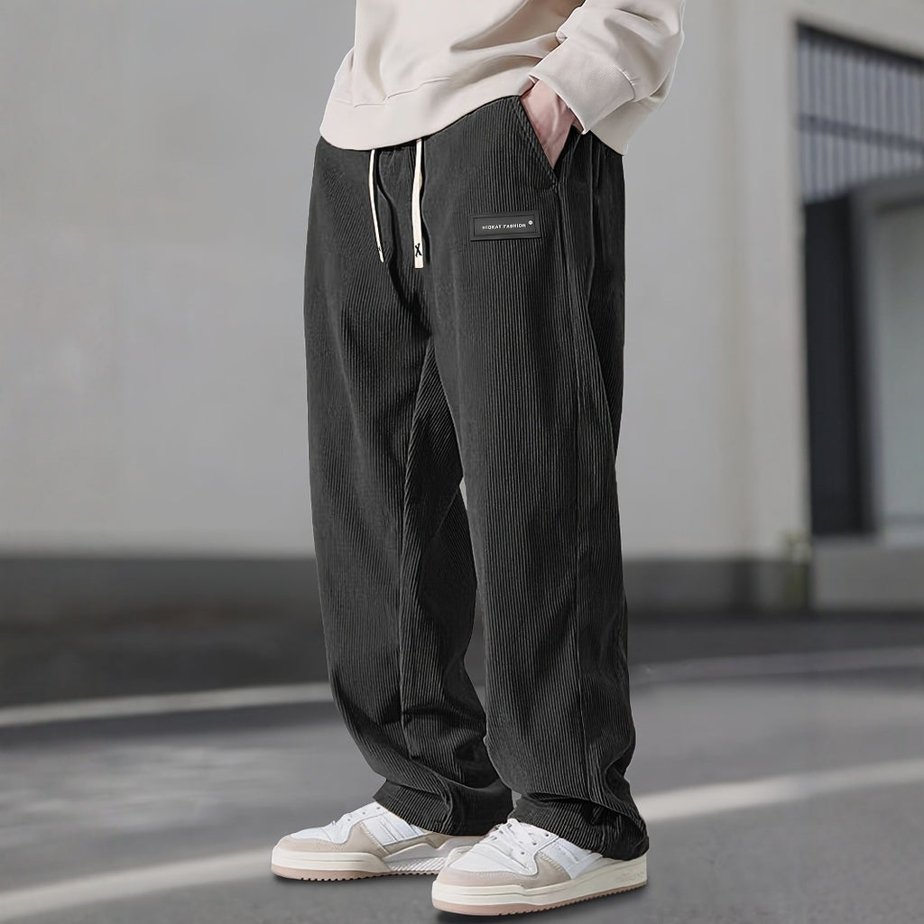 Person wearing dark corduroy pants with a light-colored hoodie in an urban setting.