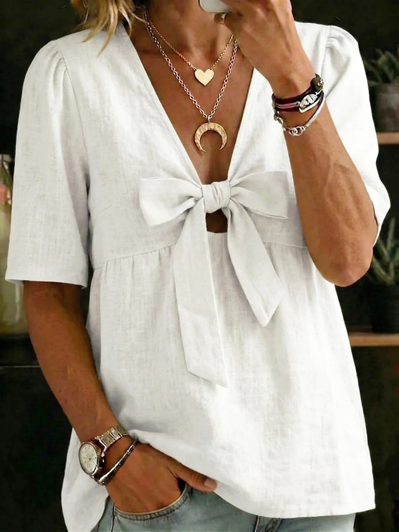 Person wearing a white blouse with a tie detail, accessorized with necklaces and bracelets.