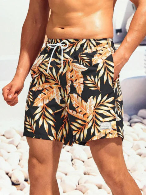 Person wearing tropical leaf patterned shorts on a pebbly beach.