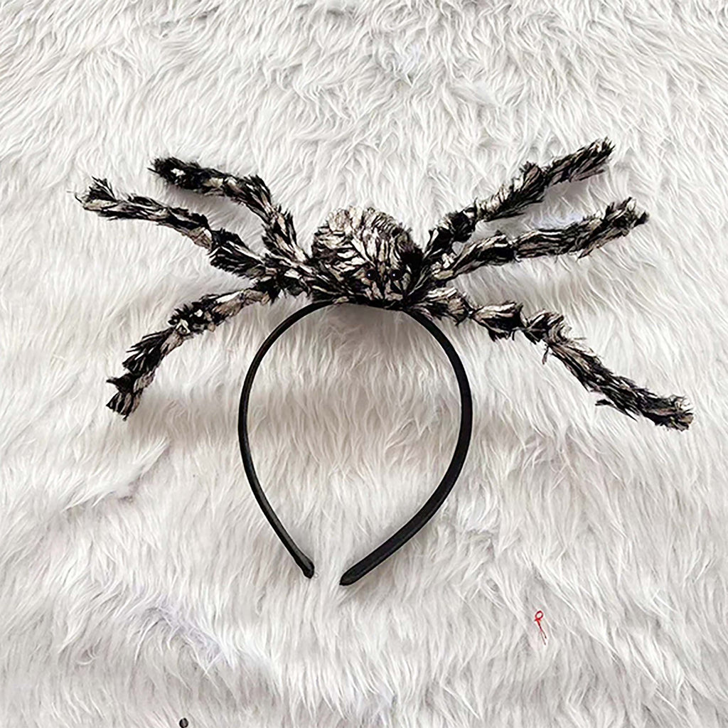 A black spider-themed headband with fluffy black and white faux-fur styled legs, laid flat on a white faux-fur background.