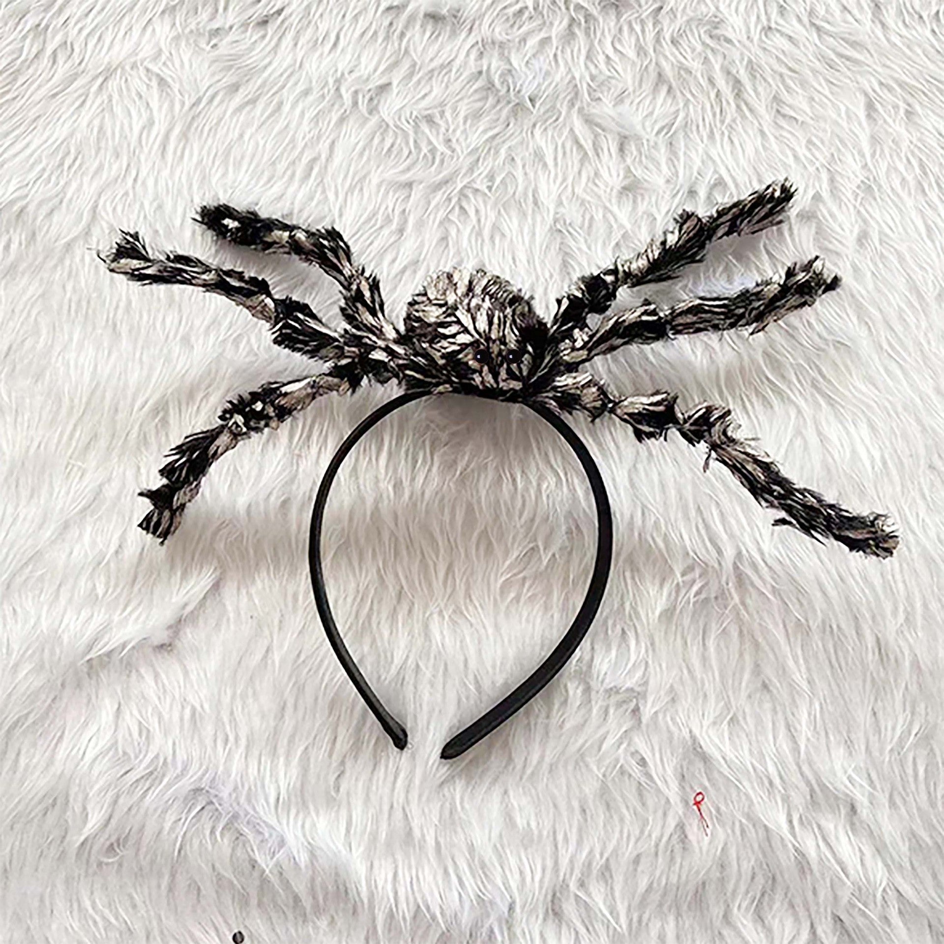A black spider-themed headband with fluffy black and white faux-fur styled legs, laid flat on a white faux-fur background.