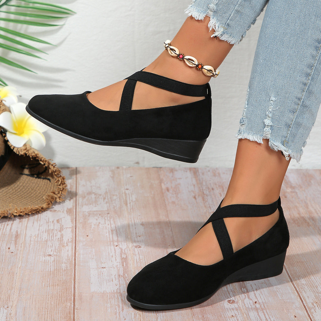 Black wedge sandals worn with light blue jeans on a wooden floor.