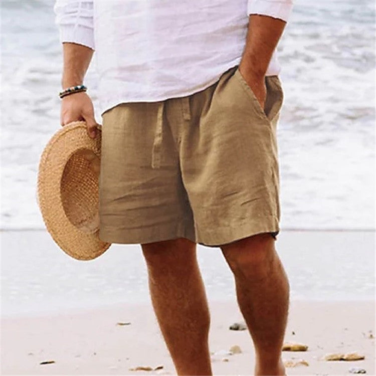 Person wearing beige shorts and holding a straw hat on a beach.