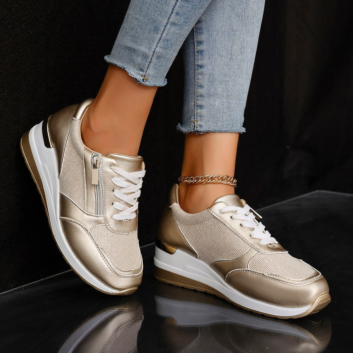 Gold sneakers with white soles worn with light blue jeans on a black background