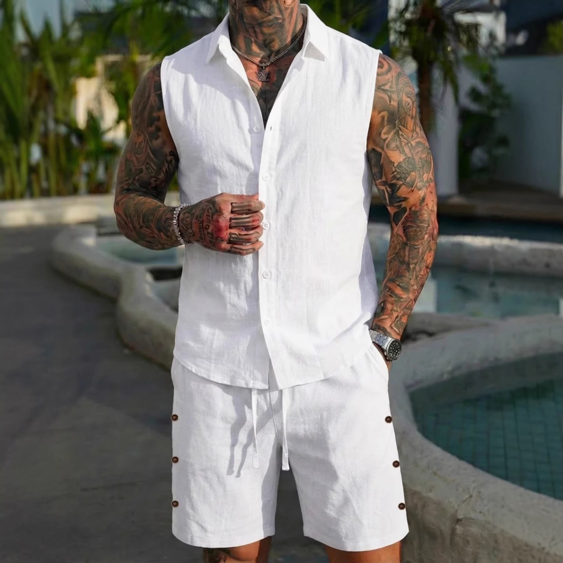 Man wearing a white vest and shorts with tattoos standing by a pool.