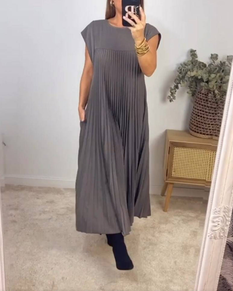 Person wearing a gray pleated dress in a room with a plant and wooden side table.