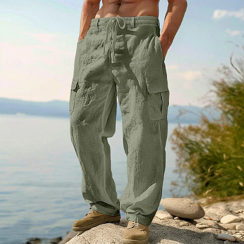 Person wearing green cargo pants standing by a body of water with mountains in the background.