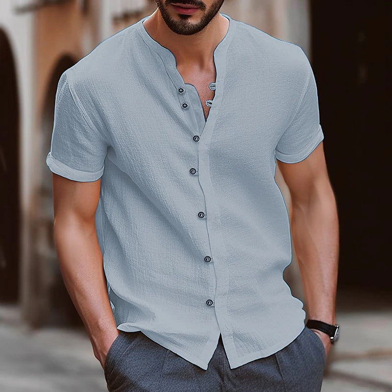 Man wearing a light gray short-sleeve button-up shirt with a blurred background