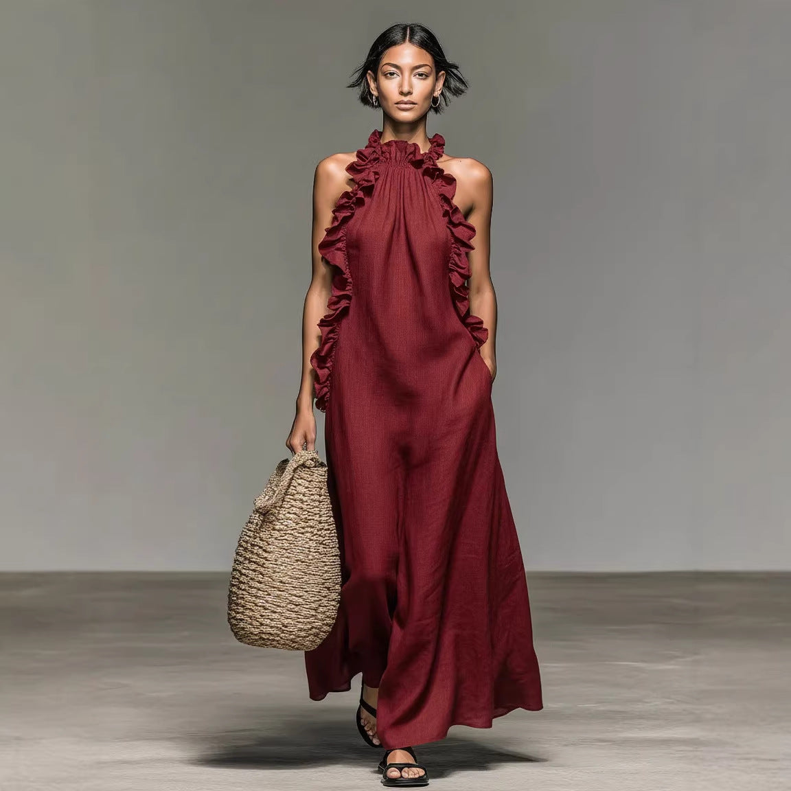 Model wearing a burgundy dress with ruffled details, holding a woven bag on a neutral background