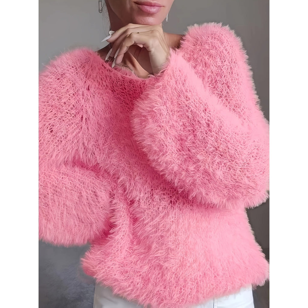 A close-up of a person wearing a bright pink, long-pile fuzzy knit sweater with voluminous balloon sleeves, paired with white pants against a neutral gray background.