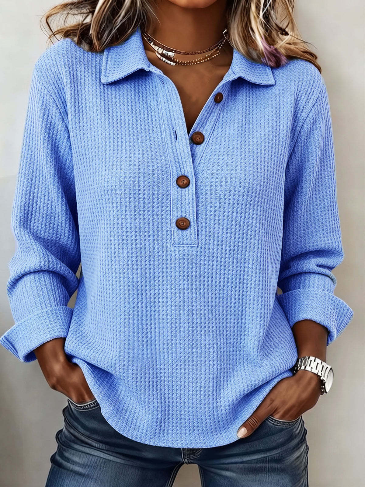 A woman wearing a light blue waffle-knit long-sleeve polo shirt with brown buttons, paired with dark blue jeans.