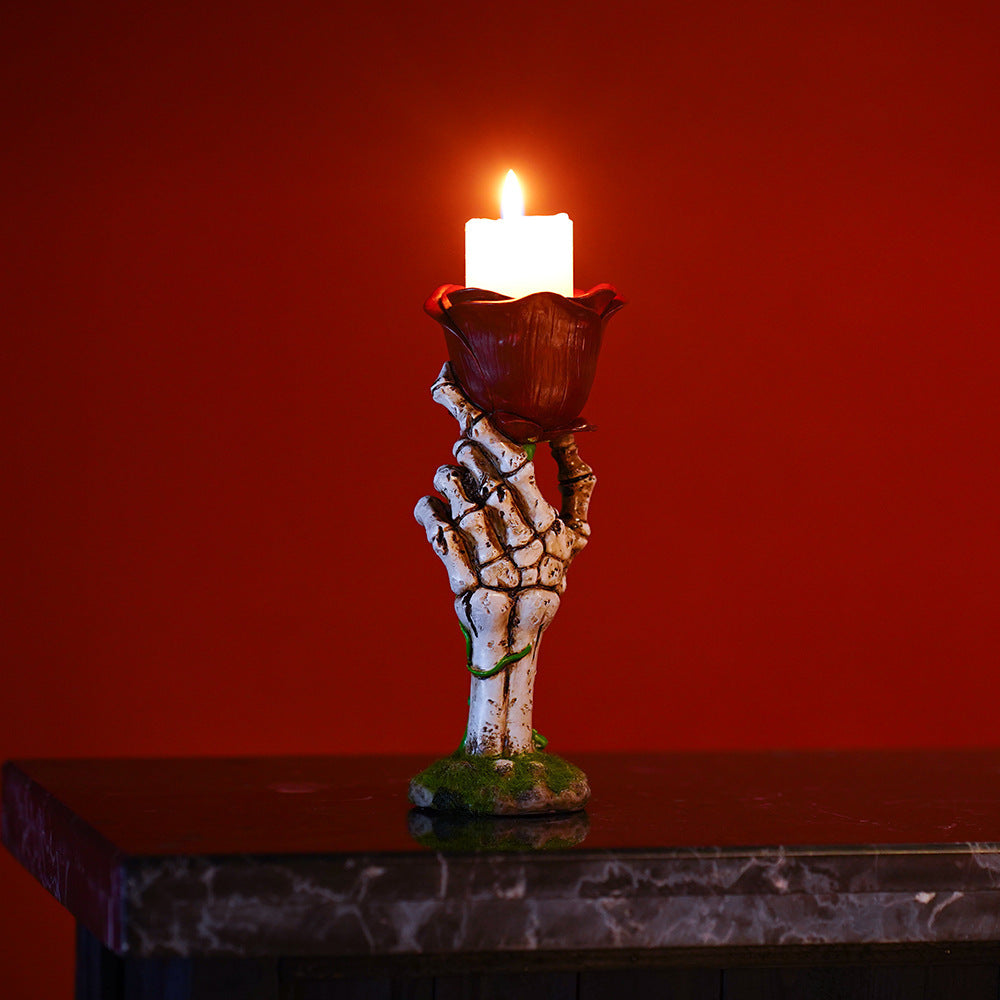 Skeleton hand candle holder with a lit candle against a red background