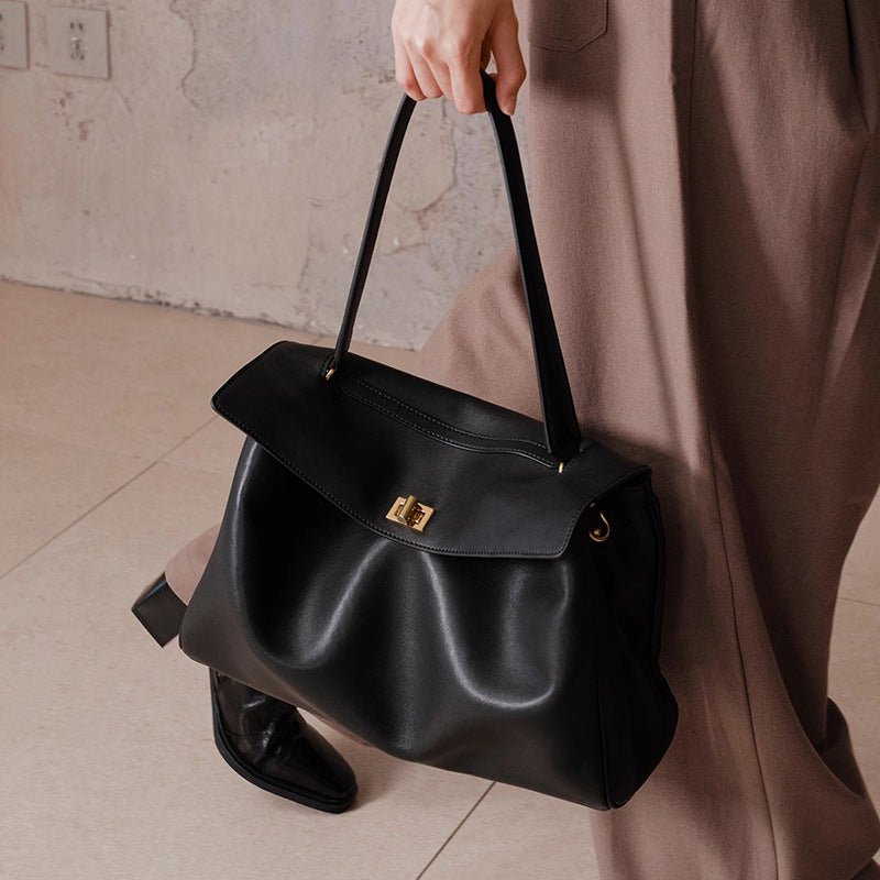 Person holding a black handbag with a neutral background