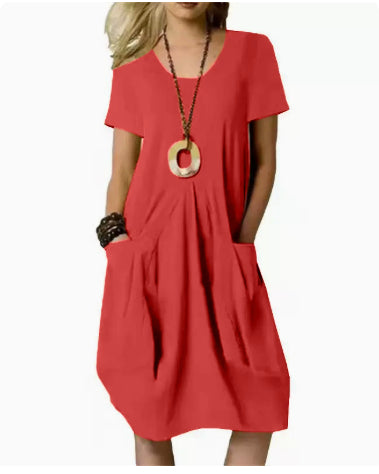 A woman wearing a short-sleeve red dress with side pockets and a V-neckline, styled with a long pendant necklace and bracelets, against a plain white background.