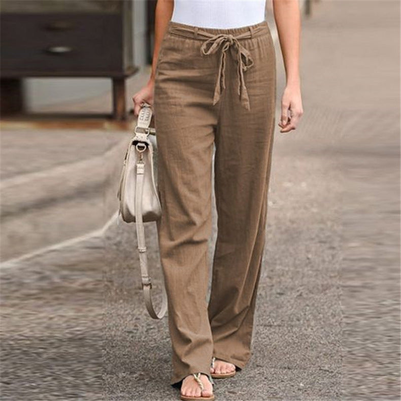 Person wearing brown drawstring pants holding a beige handbag on a blurred background