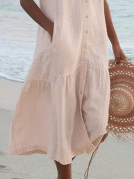 Person wearing a light pink dress holding a woven bag on a beach.