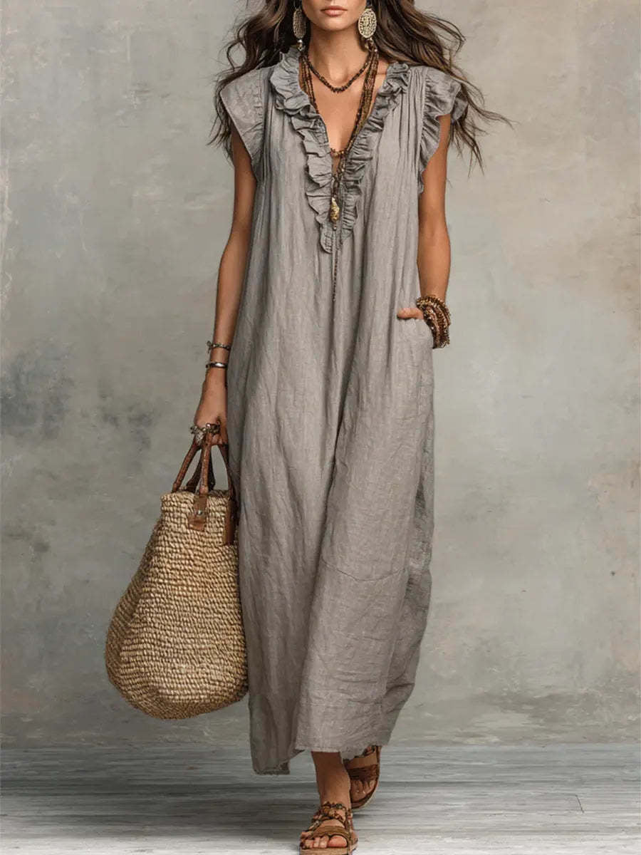 Woman wearing a long gray dress holding a woven bag against a neutral background