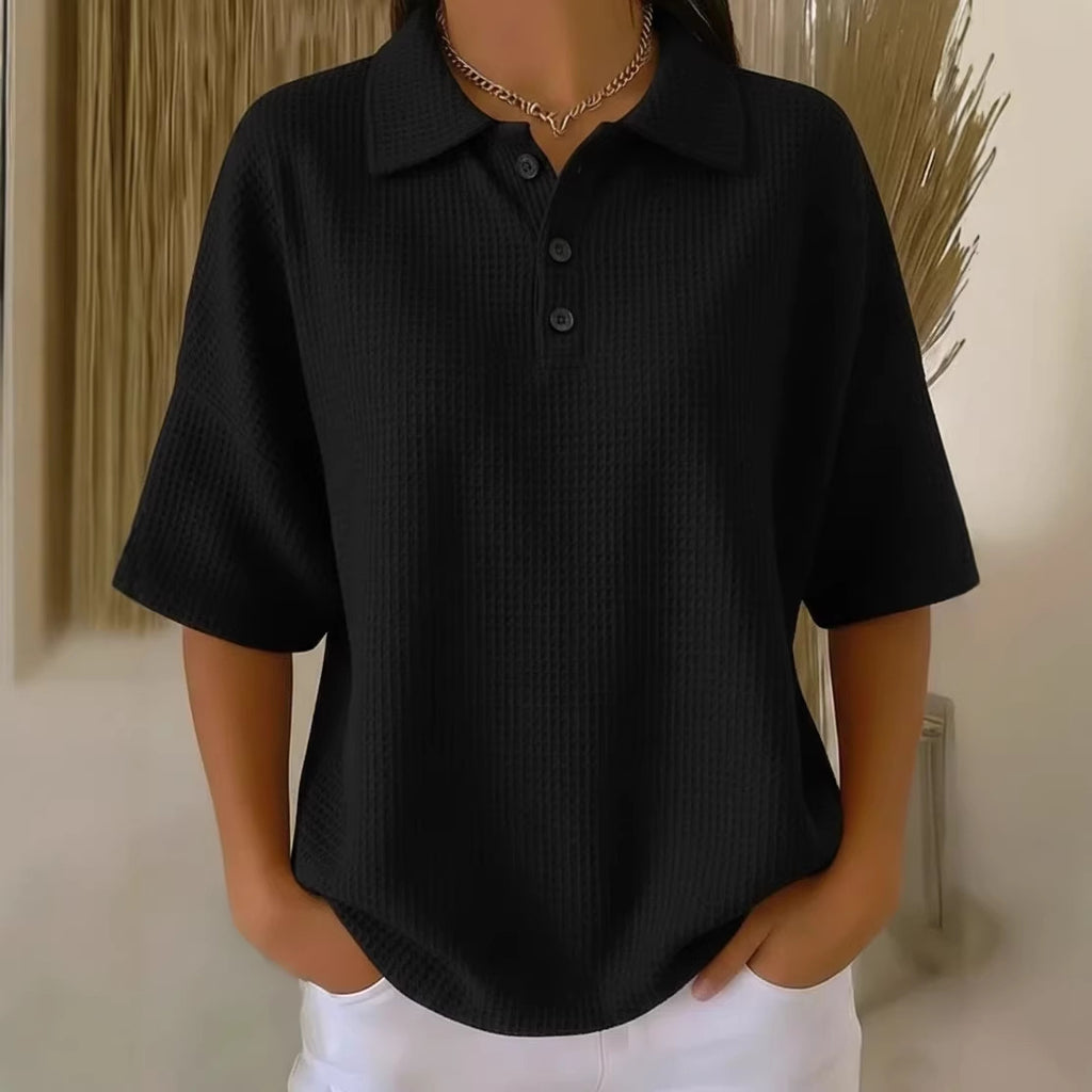 Person wearing a black short-sleeve shirt with a collar against a neutral background
