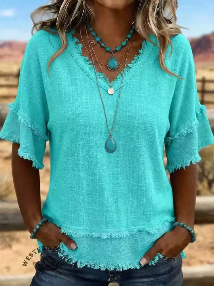 Person wearing a turquoise top with ruffled sleeves and layered necklaces outdoors.