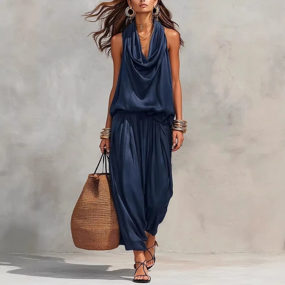 Woman wearing a navy blue sleeveless top and pants holding a woven bag against a neutral background