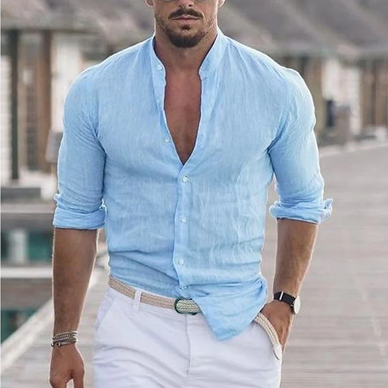 Man wearing a light blue button-up shirt with rolled-up sleeves and white pants outdoors.