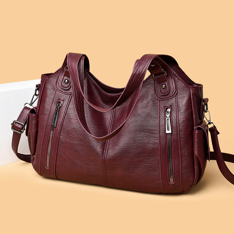 Brown leather handbag with zippers on a beige background