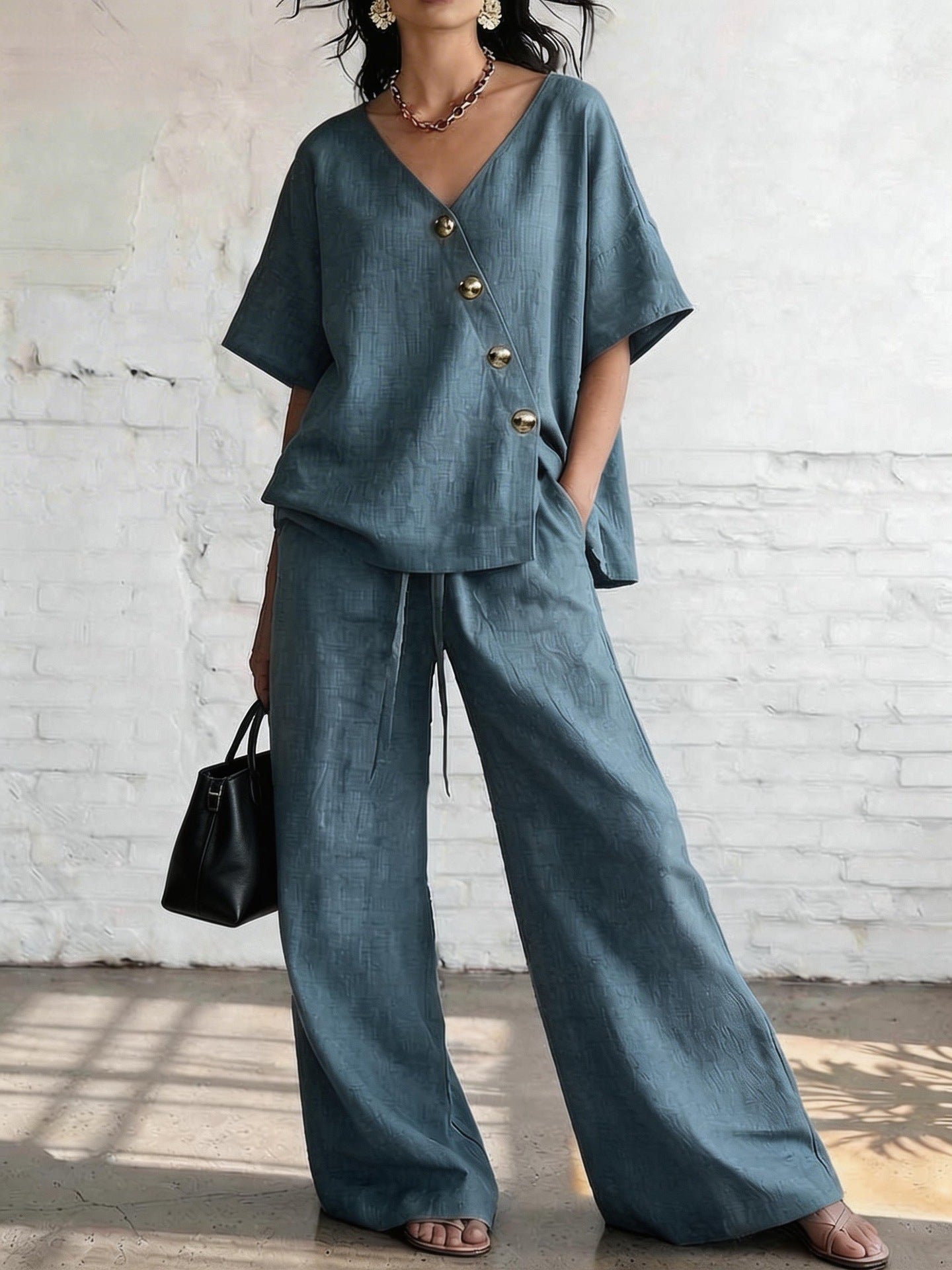 Person wearing a blue outfit with wide-leg pants against a white brick wall.