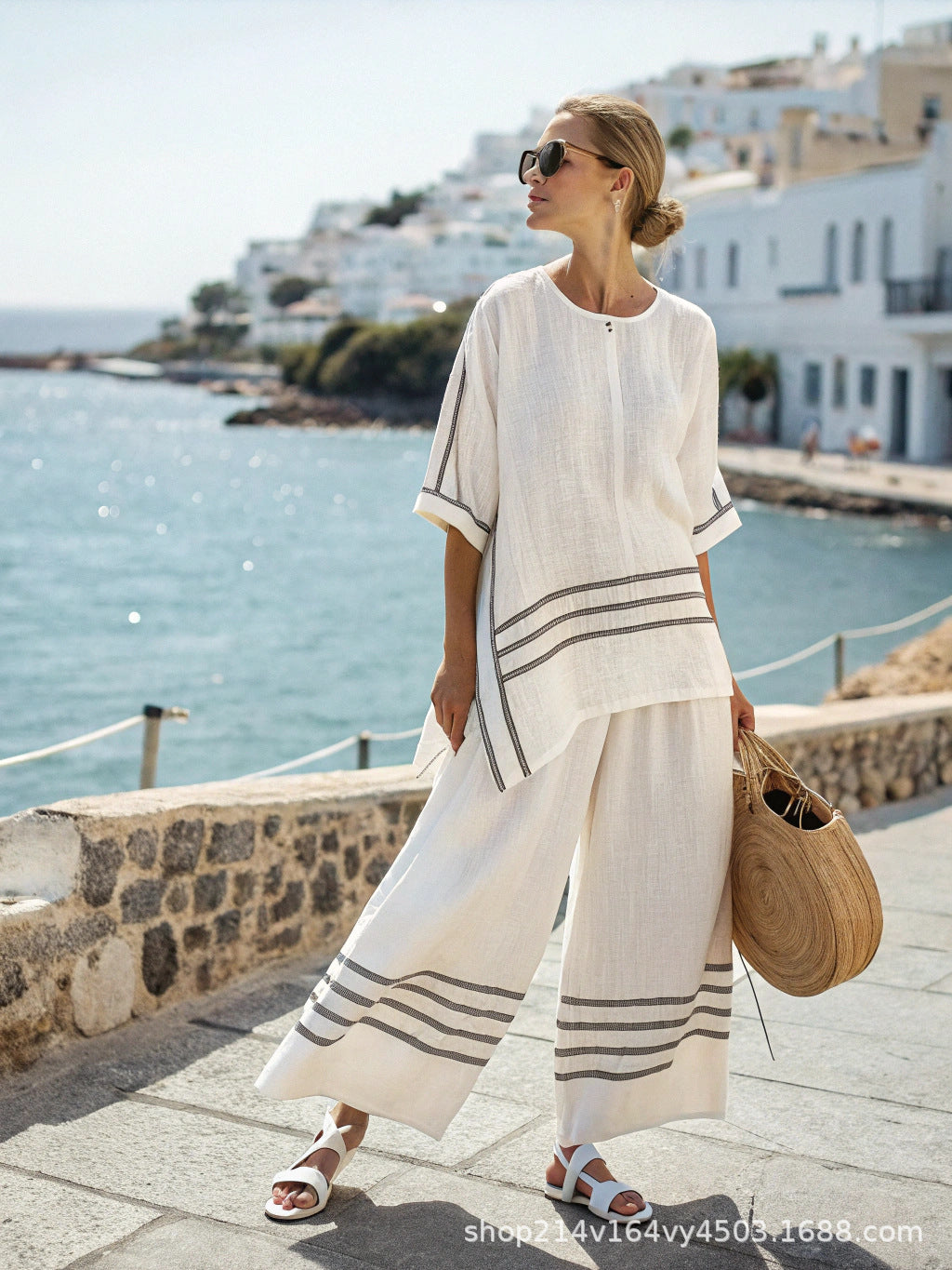 Woman in a white outfit with black stripes standing by a waterfront with white buildings in the background.
