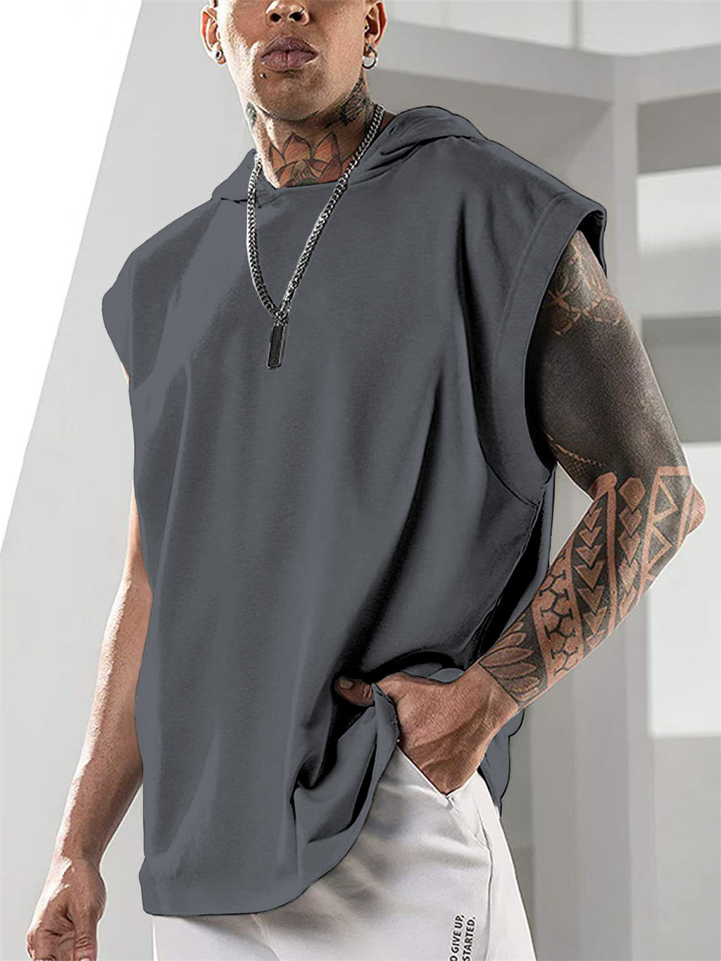 Person wearing a sleeveless gray top with tattoos on arms, standing against a light background