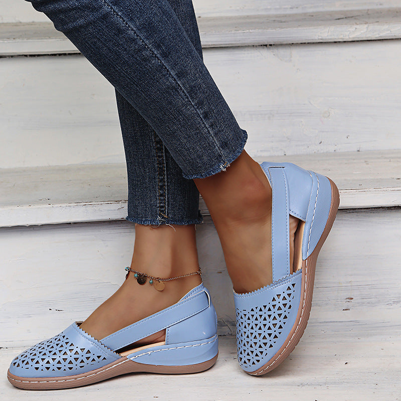 Light blue sandals with brown soles worn by a person sitting on a wooden bench.