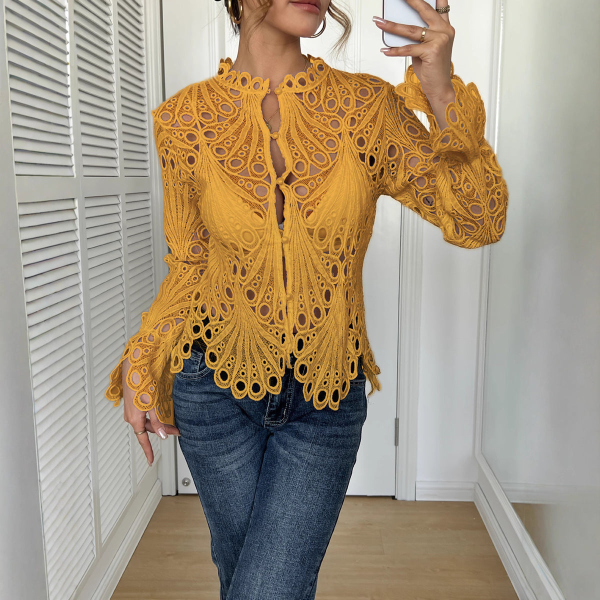 Person wearing a mustard yellow lace top and blue jeans indoors.