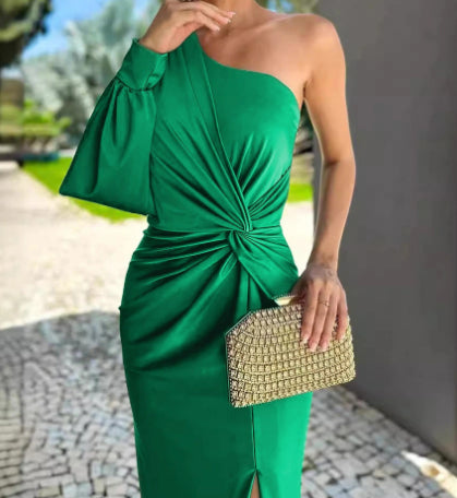 Woman wearing a green one-shoulder dress holding a gold clutch outdoors.