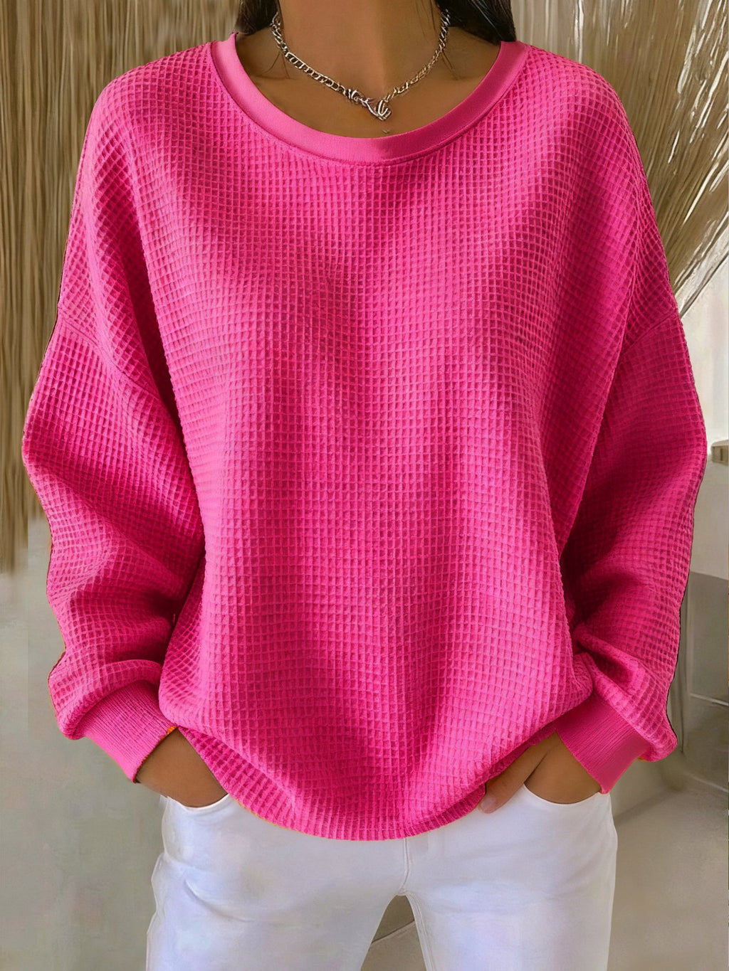 Person wearing a bright pink textured sweater and white pants indoors.
