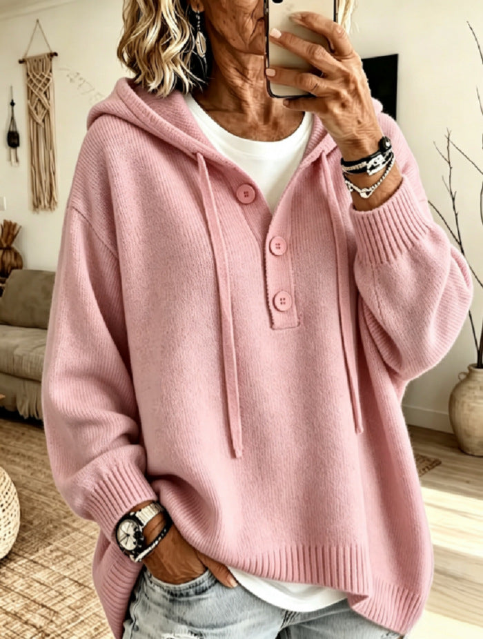 A woman takes a mirror selfie wearing a pink knit hooded sweater with drawstrings and a three-button placket over a white top and light-wash jeans.