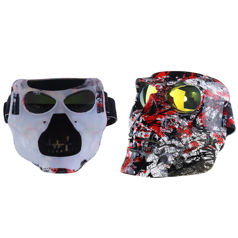 Two tactical face masks with integrated goggles shown side by side on a plain white background. The left mask is white with red splatter and black details, and the right mask is black, white, and red splatter with bright yellow lenses.