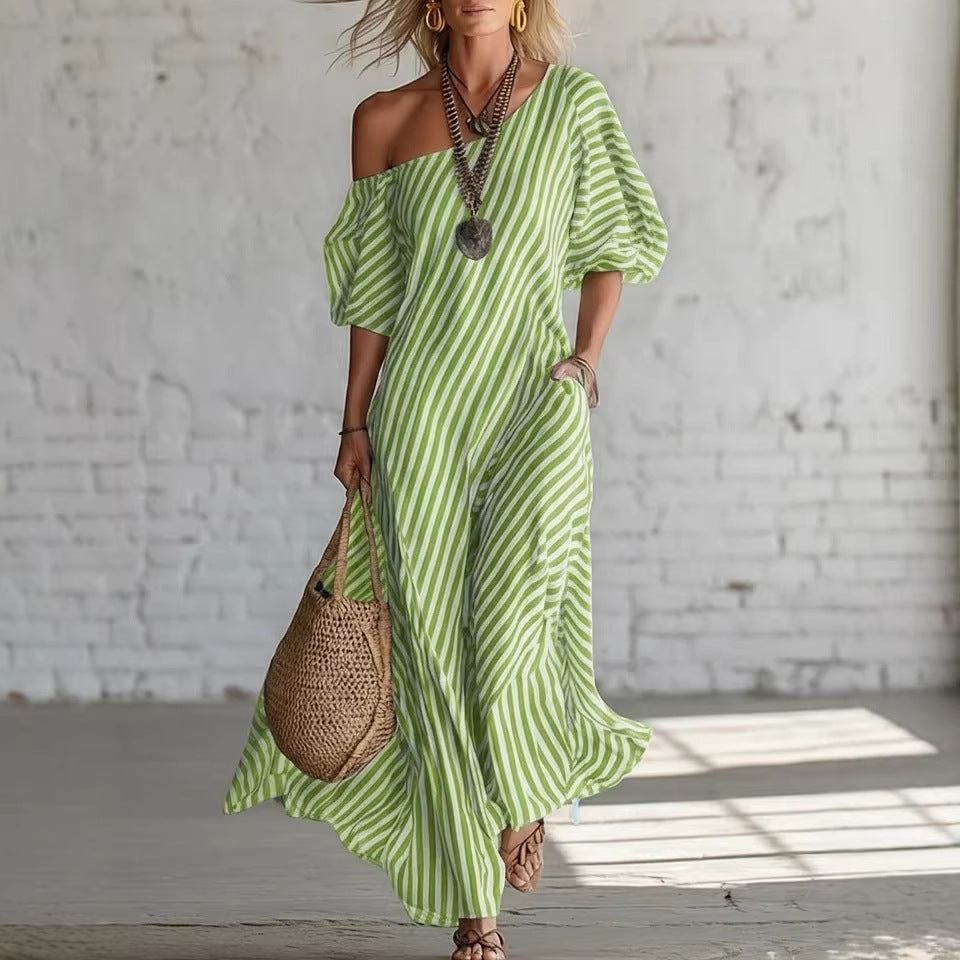 Woman wearing a green and white striped dress holding a woven bag against a white brick wall.