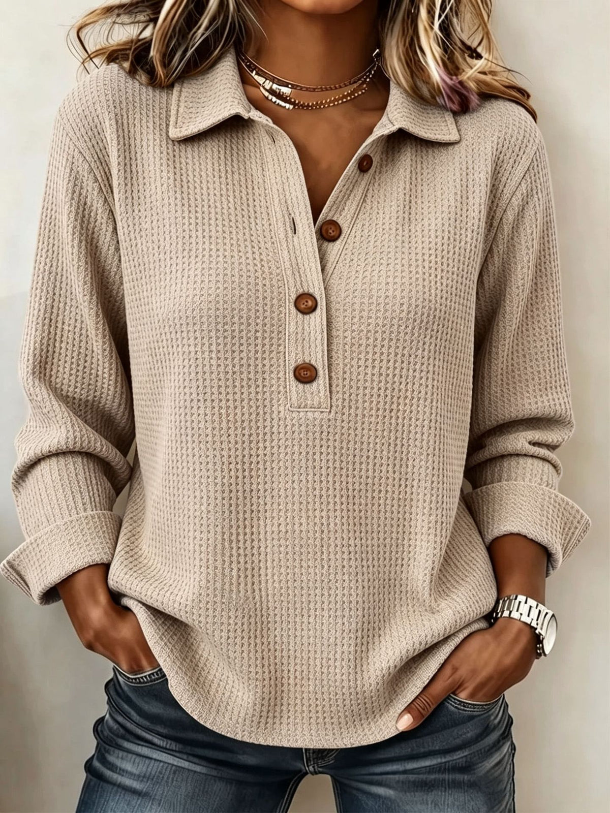 A woman wearing a beige waffle-knit long-sleeve polo shirt with brown buttons, paired with blue jeans, shown from the neck down against a neutral background.