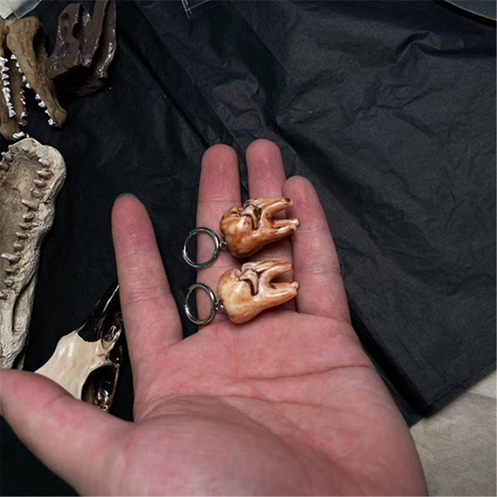 Hand holding two small gold teeth with rings on a dark background