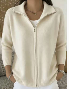 A woman wearing a cream-colored ribbed knit zip-up cardigan sweater over a white top, shown from the neck down in a close-up shot.