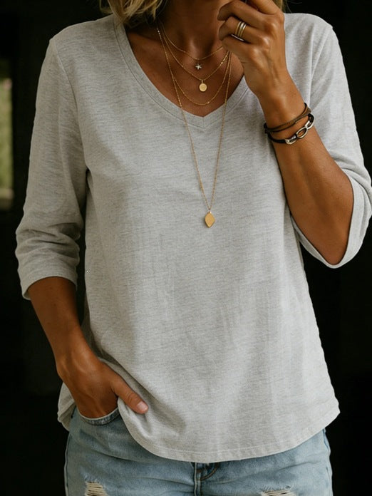 Person wearing a gray long-sleeve shirt and light blue jeans with layered necklaces and bracelets.