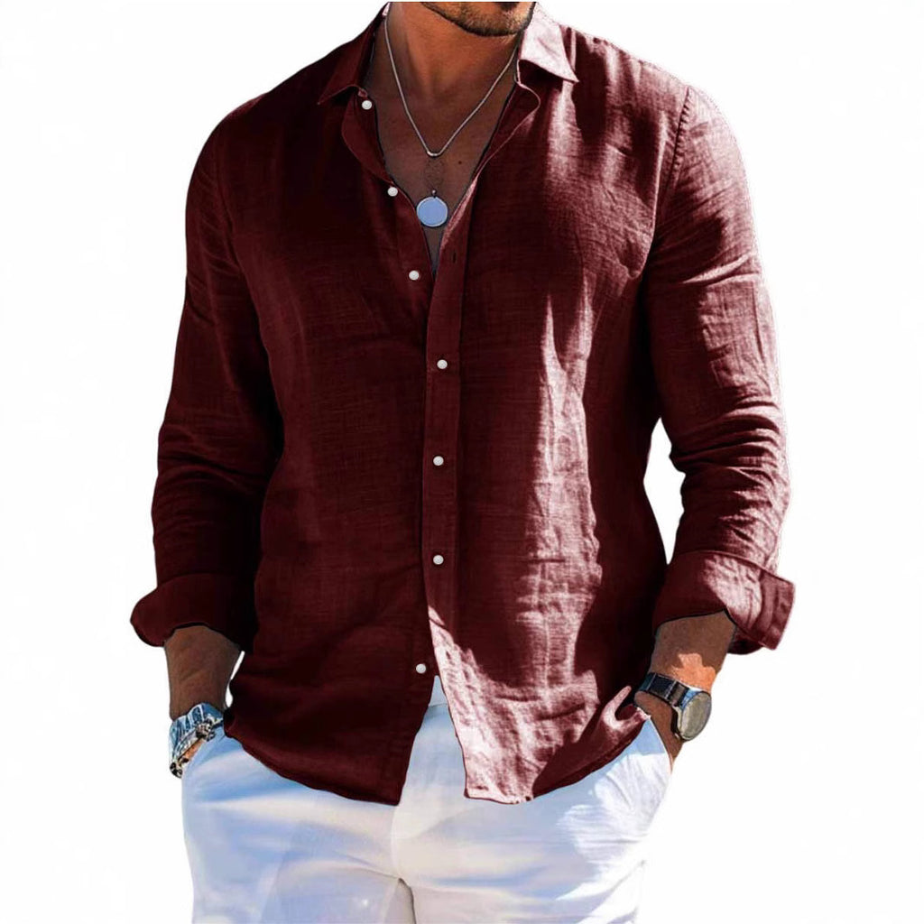 Man wearing a maroon shirt and white pants standing on a beach.