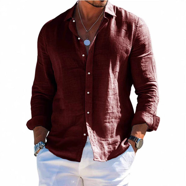 Man wearing a maroon shirt and white pants standing on a beach.