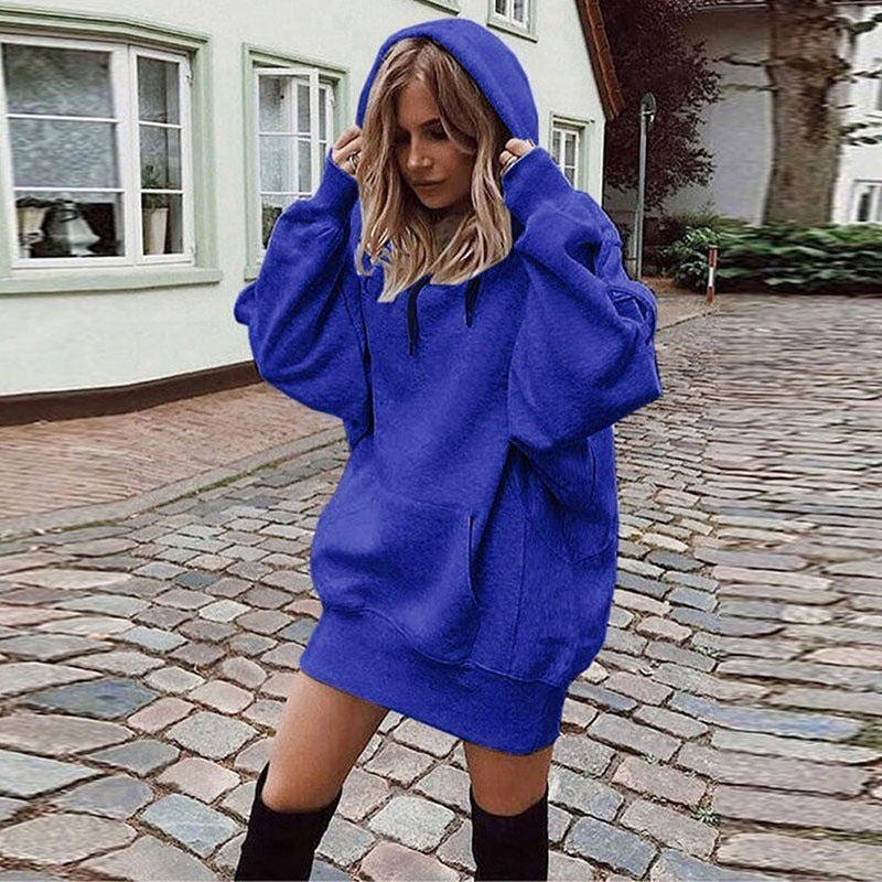 A woman wearing an oversized royal blue hoodie sweatshirt dress with black knee-high socks, standing on a cobblestone street in front of a light-colored building.