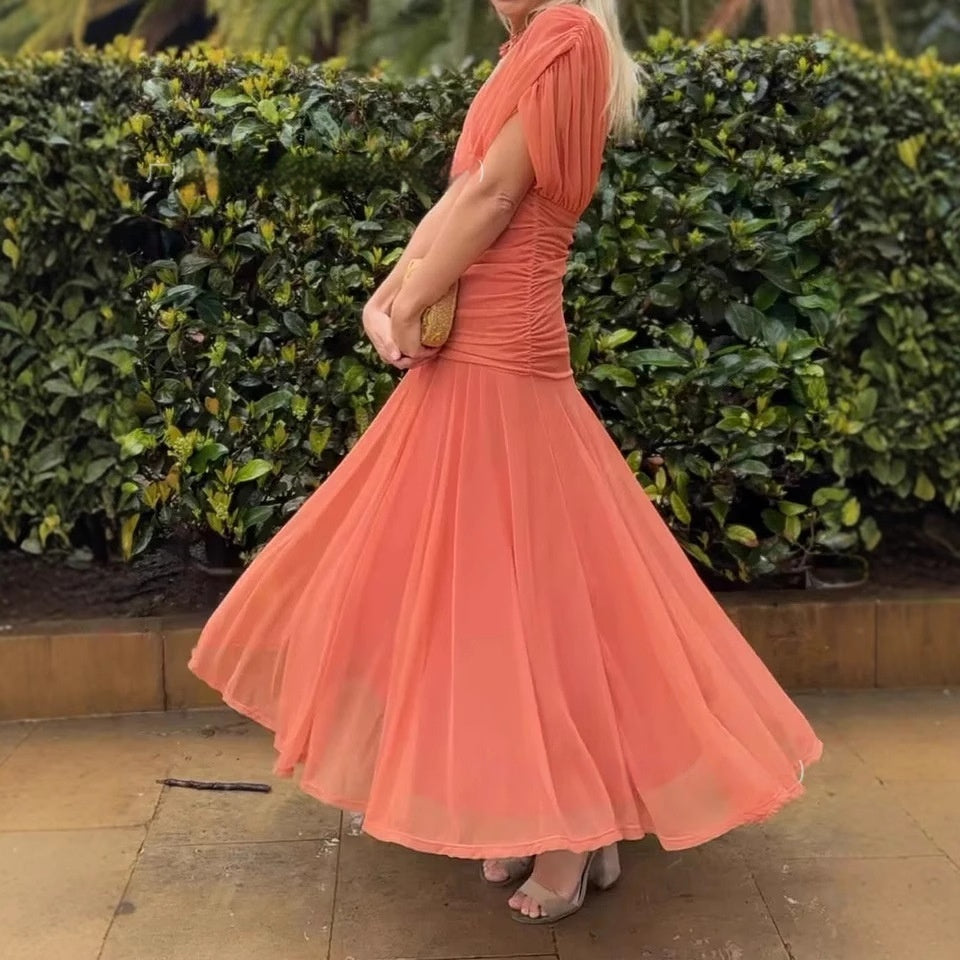 Woman in an orange dress standing in front of green bushes