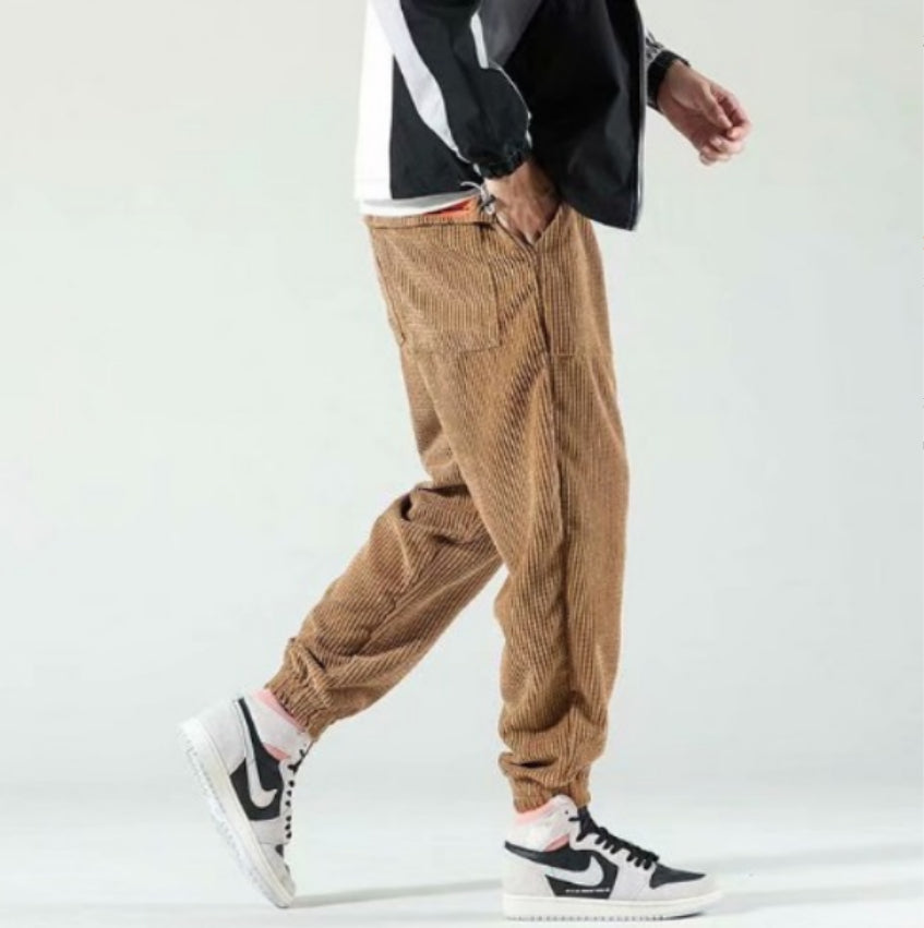 Person wearing brown corduroy pants and black and white sneakers on a light gray background