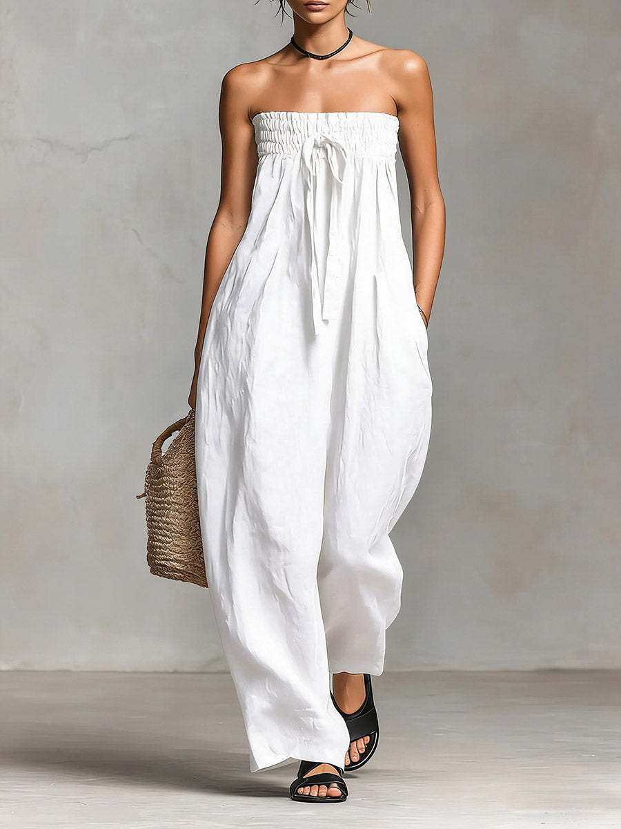 Woman wearing a white strapless dress holding a woven bag against a plain background